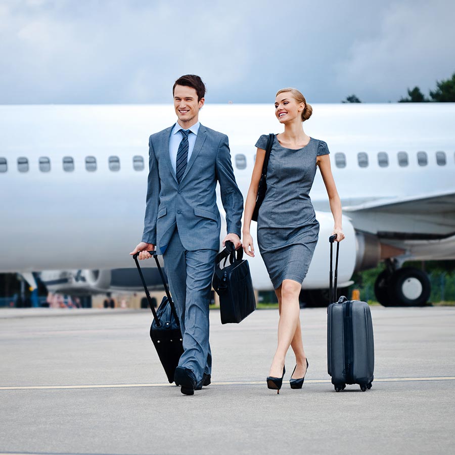 A man and woman in business attire walk with luggage away from a private jet