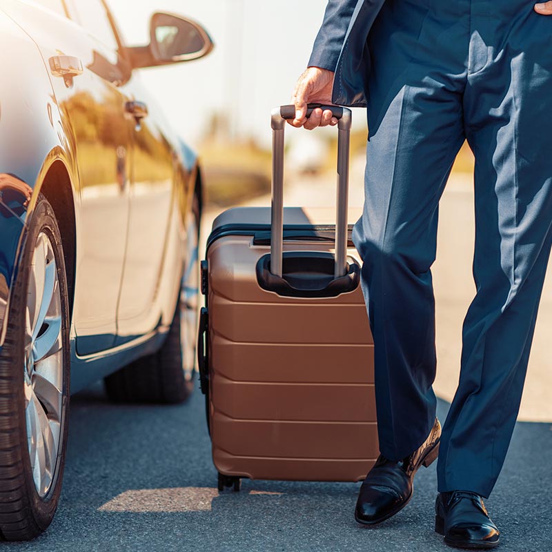 A business man exits a nice car with luggage in tow