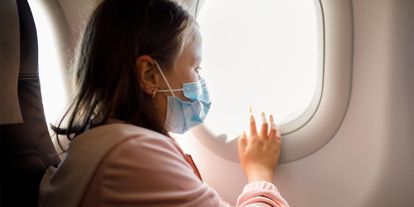 Girl staring out airplane window wearing a mask